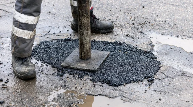 worker pushing bitumen asphalt in the hole. road repair and maintenance