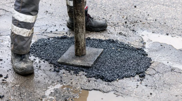 worker pushing bitumen asphalt in the hole. road repair and maintenance